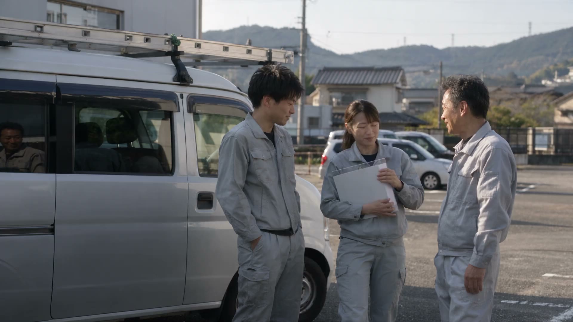 作業着の3人が白い軽バンの前で話している(仮の写真)